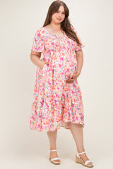 woman wearing a pink floral smocked maternity dress with short sleeves and pockets, holding her baby bump