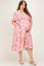 woman wearing a pink floral smocked maternity dress with short sleeves and pockets, holding her baby bump