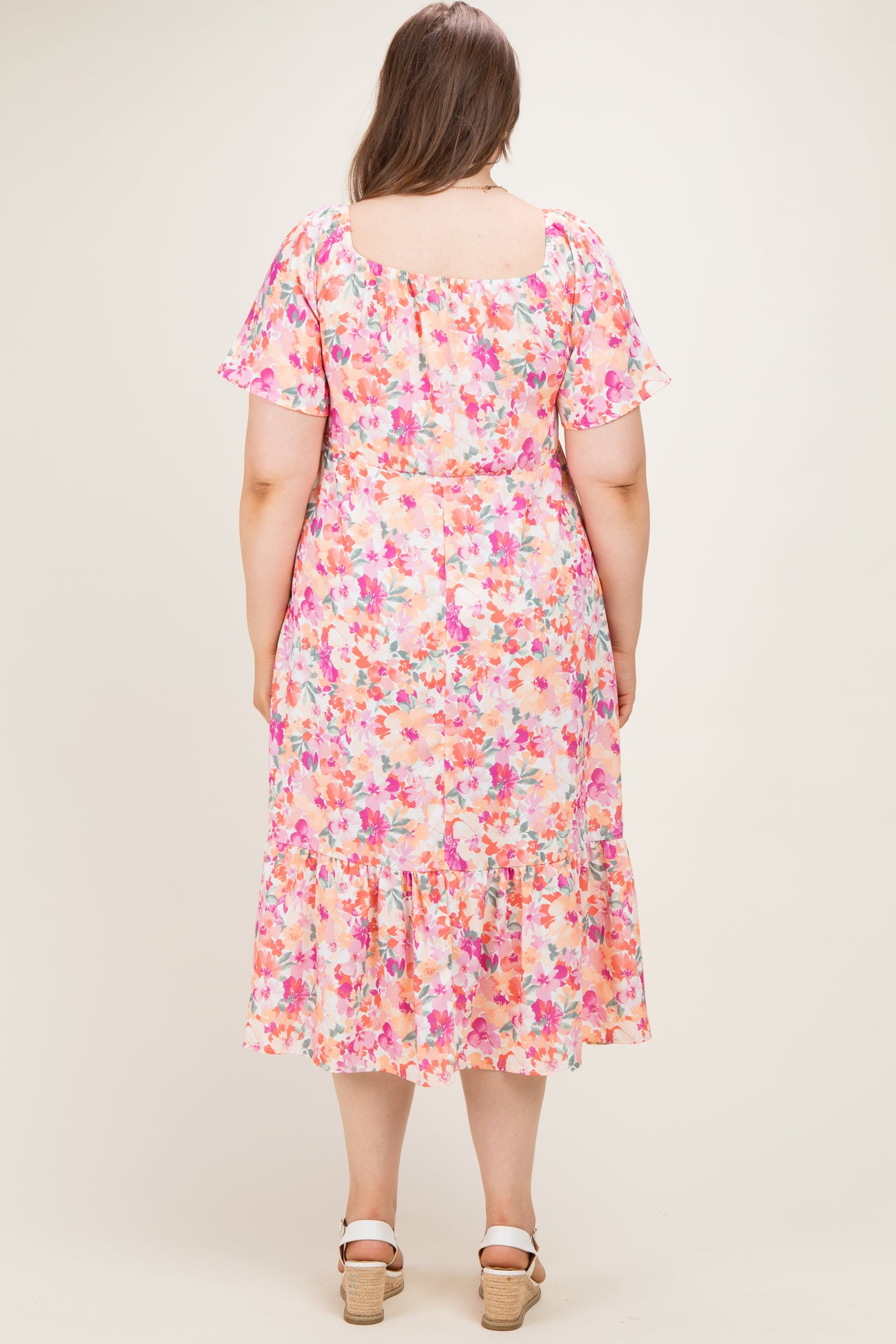 woman wearing a floral maternity plus dress with short sleeves and a tiered hem, shown from the back