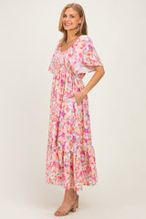 woman wearing a floral pink maxi dress with short sleeves and pockets, standing and smiling on a neutral background