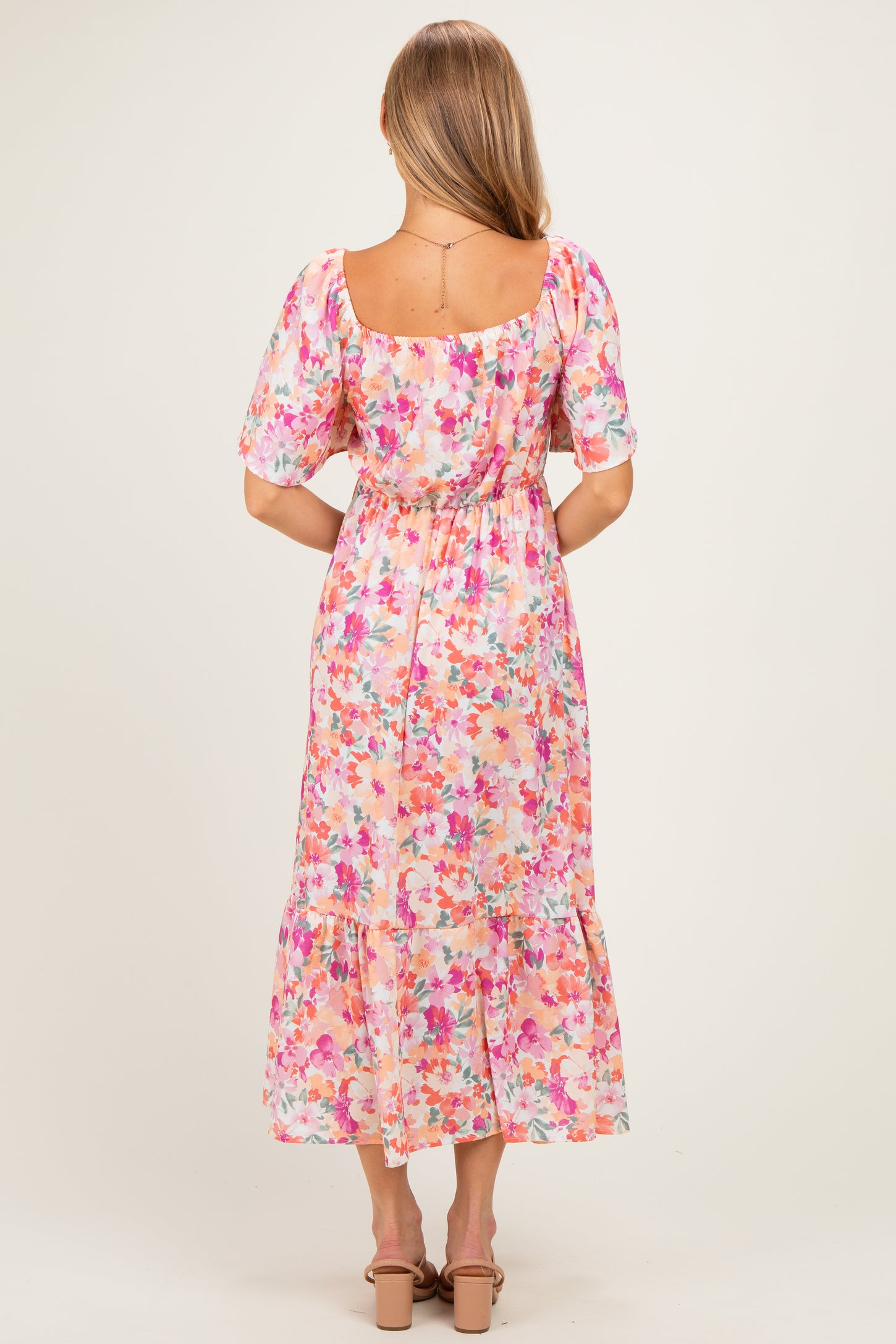 woman wearing a floral pink midi dress with puff sleeves and a tiered hem, viewed from the back
