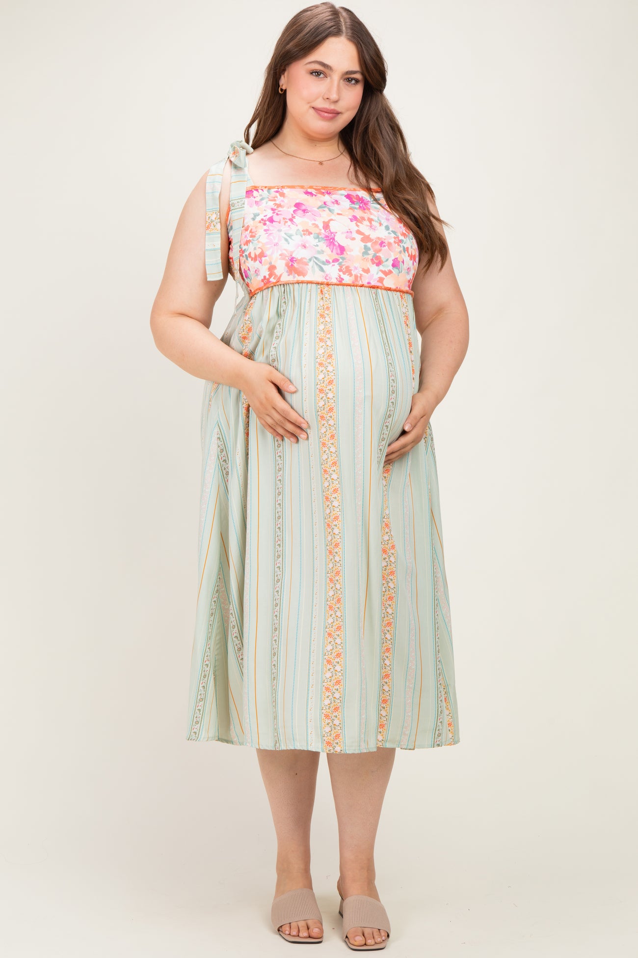 woman wearing a floral and striped maternity maxi dress with a tied shoulder and holding her baby bump