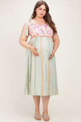woman wearing a floral and striped maternity maxi dress with a tied shoulder and holding her baby bump