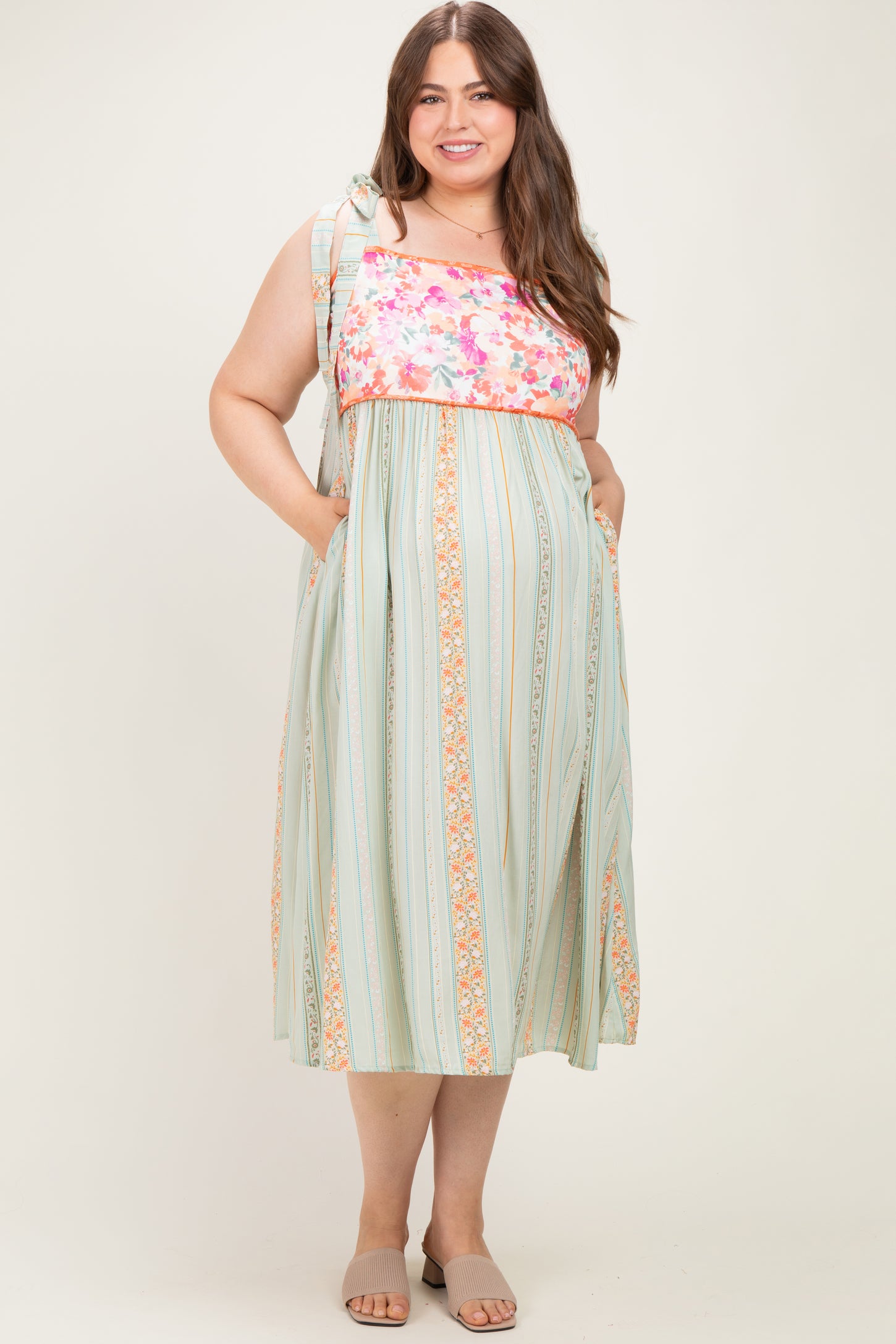 woman wearing a floral print maternity plus maxi dress with ruffled straps and side pockets, featuring a striped pattern and a baby bump