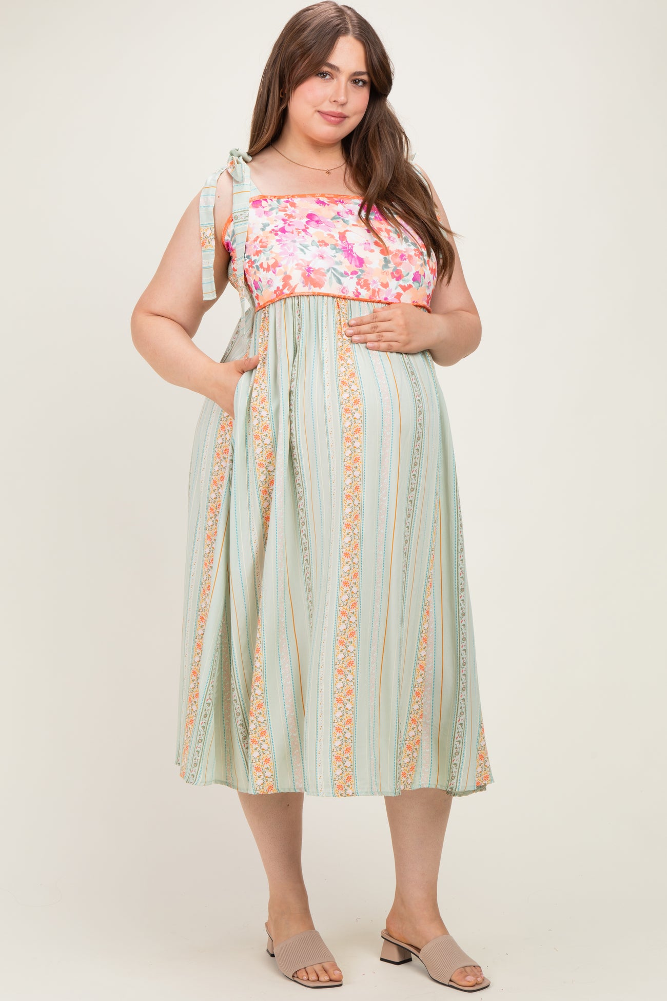 woman wearing a floral and striped maternity dress with tie straps and pockets, featuring a visible baby bump