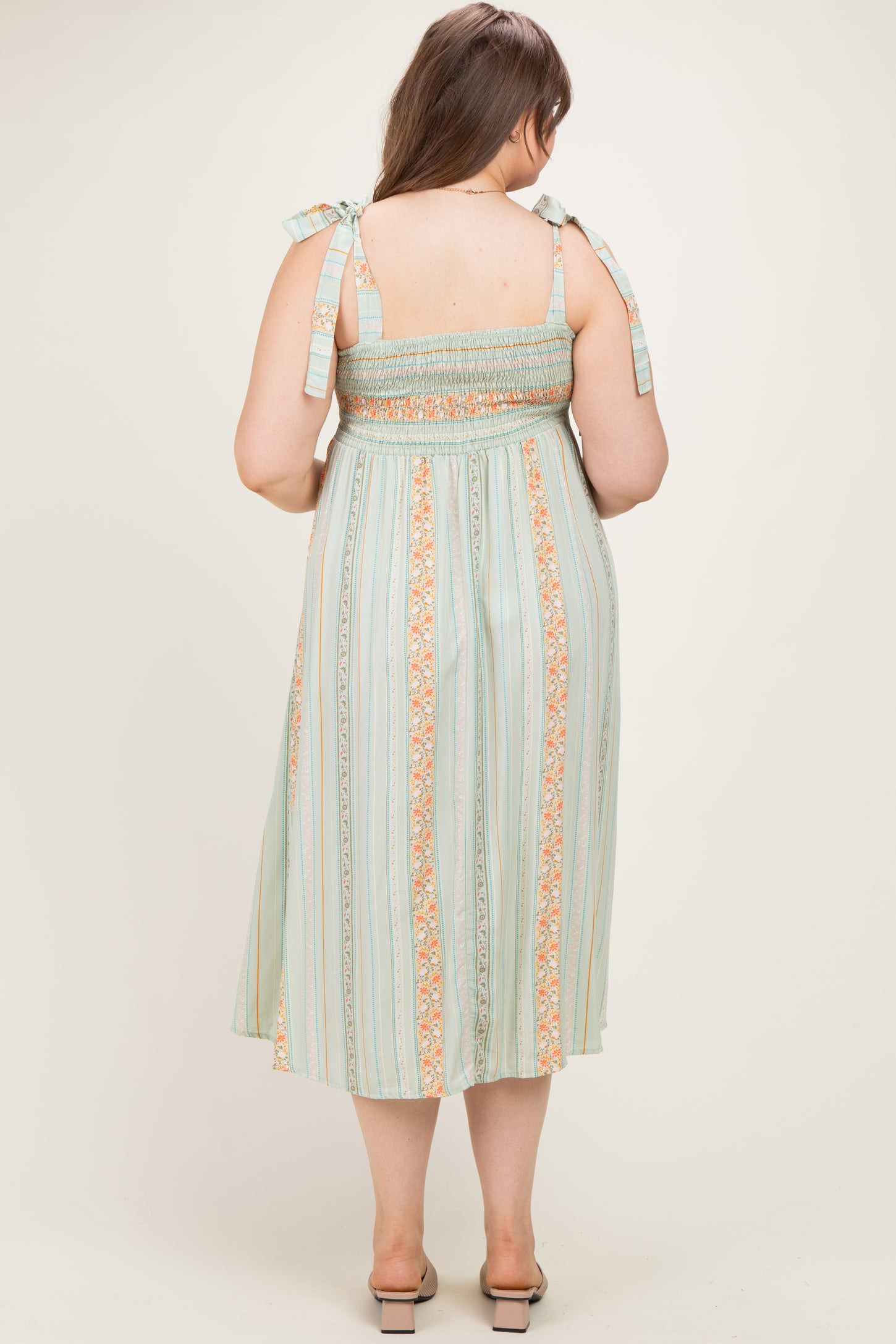 woman wearing a green and orange striped maternity dress with smocked bodice and tie straps, showing a baby bump from the back