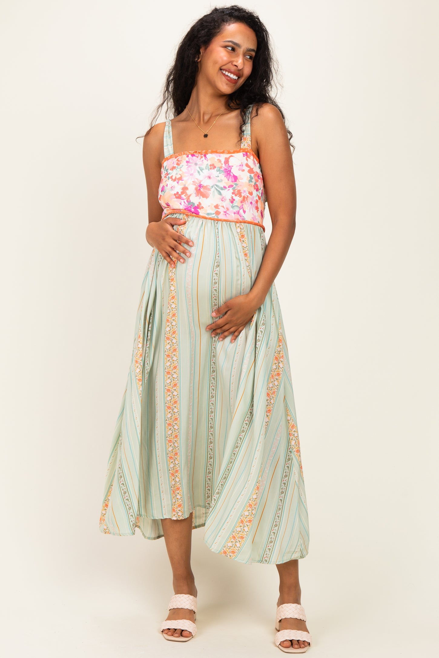 woman wearing a floral print maternity dress with a fitted bodice and flowy skirt, posing with baby bump visible