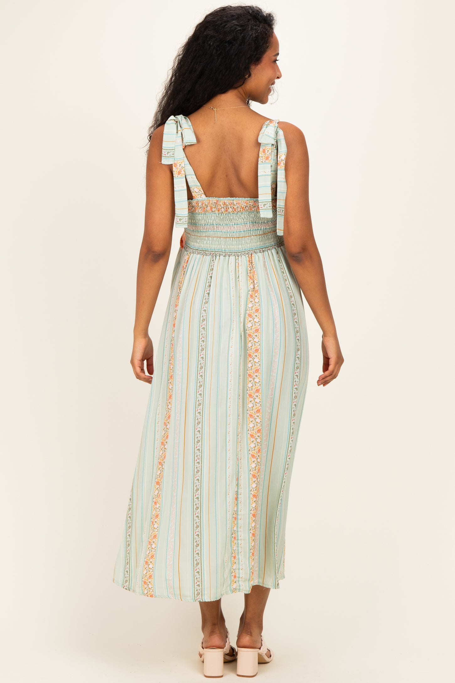 woman wearing a mint green maternity dress with smocked bodice and ribbon straps, showing a flowing skirt from the back