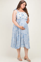 woman wearing a light blue floral maternity dress with a tie shoulder, gently cradling her baby bump