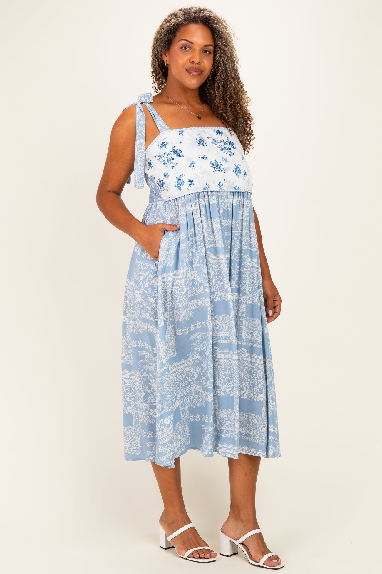 woman wearing a light blue floral plus size midi dress with adjustable tie straps and pockets