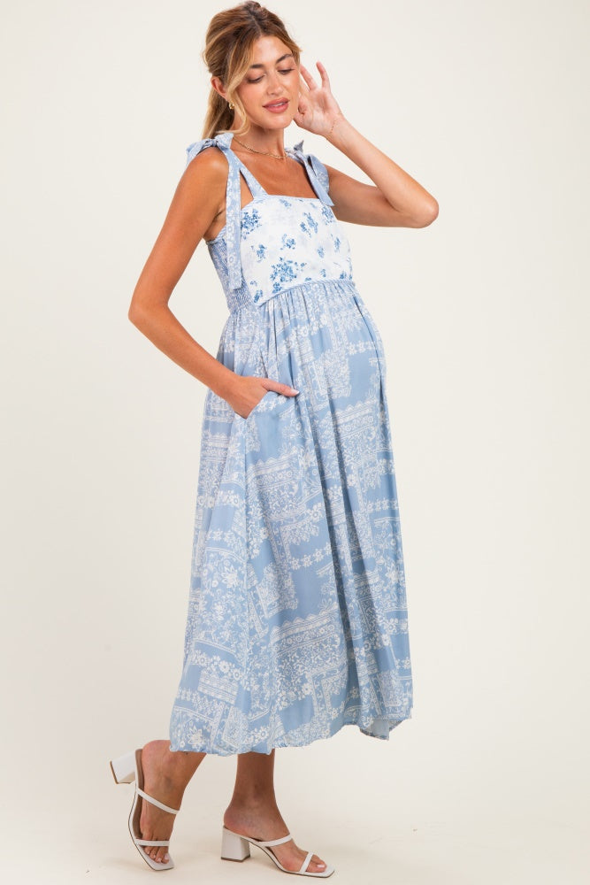 woman wearing a light blue floral maternity dress with tie straps and pockets, showcasing her baby bump