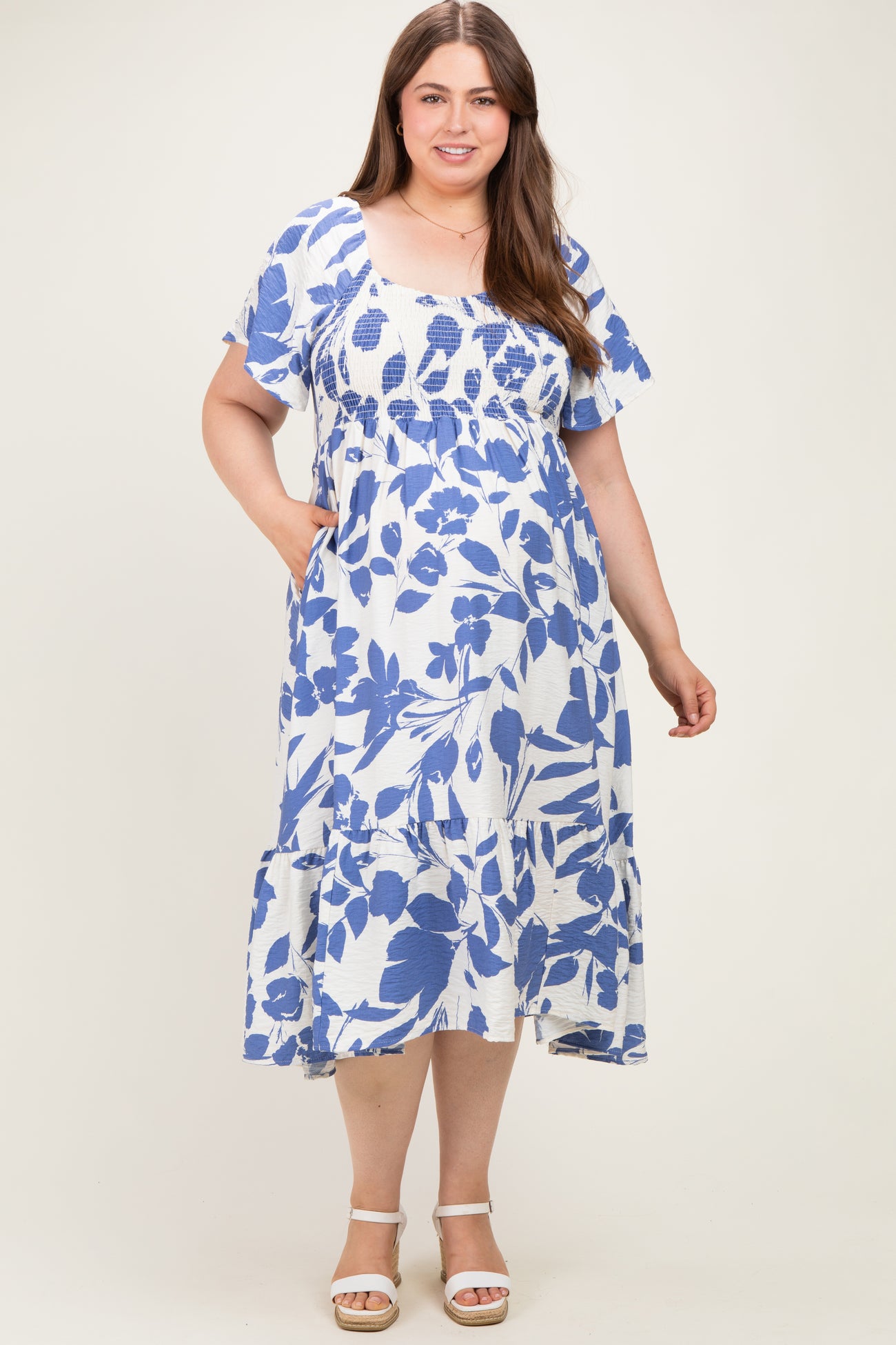 woman wearing a white and blue floral print maternity dress with short sleeves and pockets in a flowing style