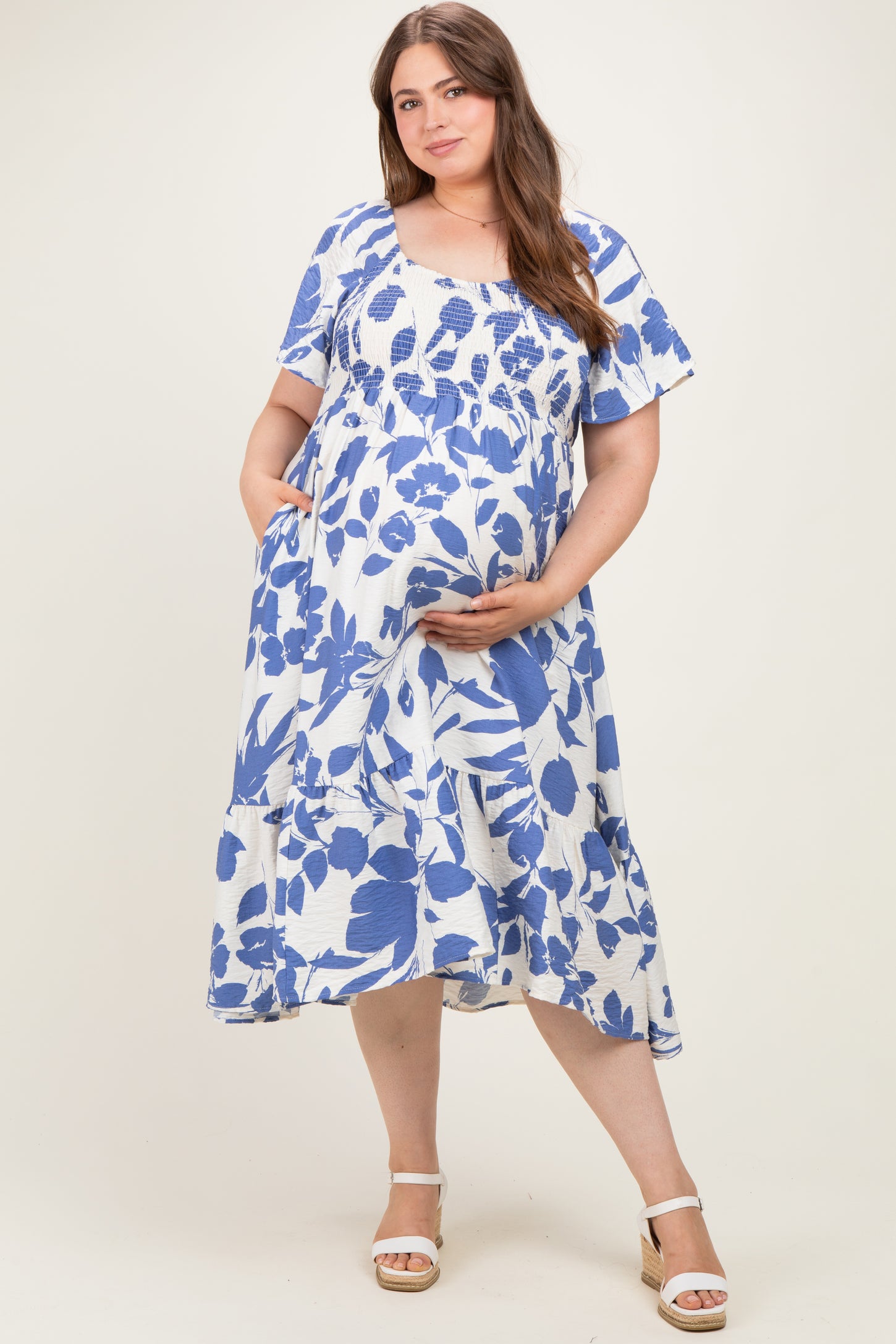 woman wearing a blue and white floral short sleeve maternity dress with a smocked bodice and a visible baby bump