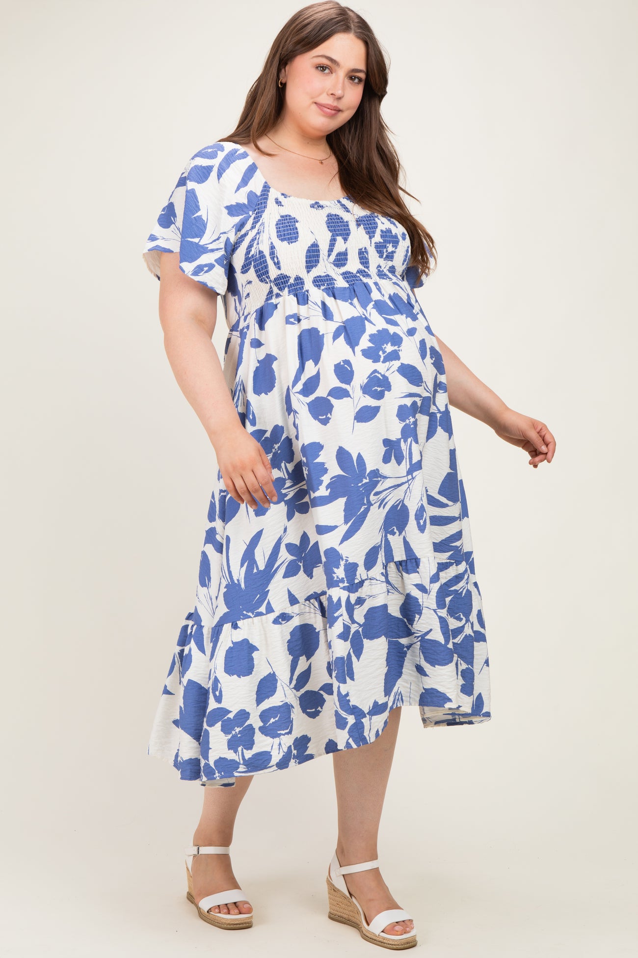 woman wearing a blue and white floral maternity plus dress with a smocked bodice and tiered skirt, showing her baby bump