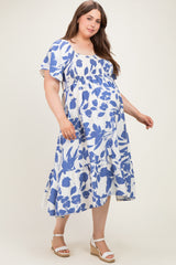 woman wearing a blue and white floral maternity plus dress with a smocked bodice and tiered skirt, showing her baby bump