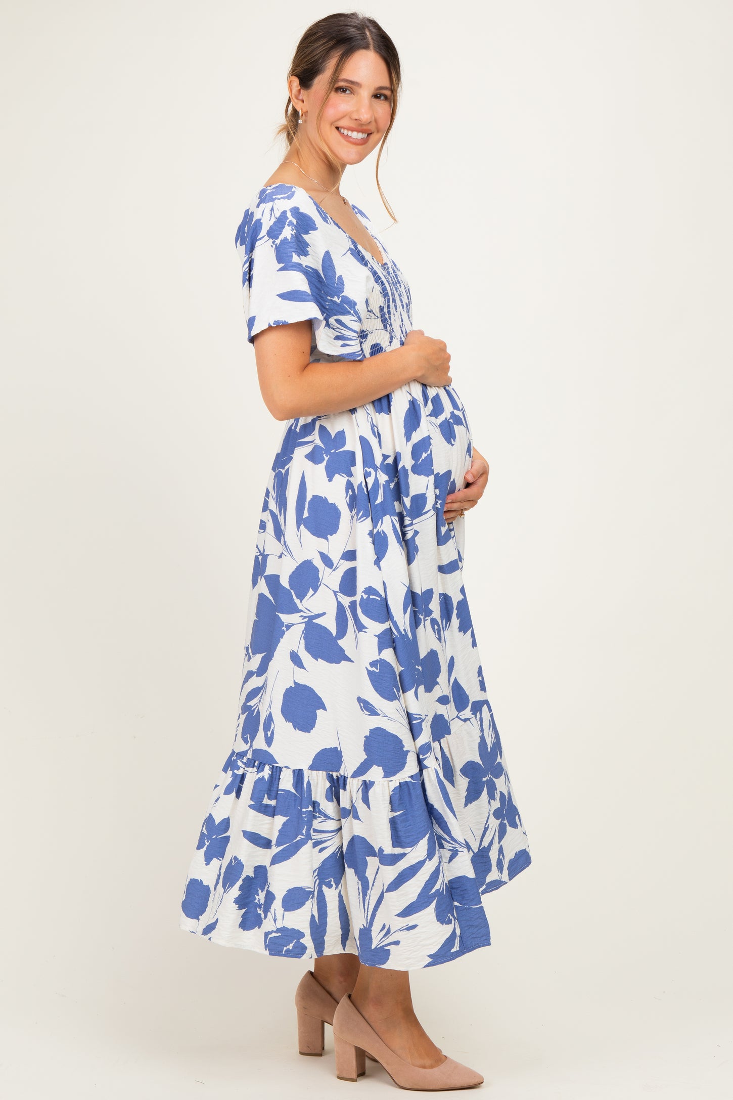 woman wearing a blue and white floral maternity dress with a tiered skirt, showcasing her baby bump