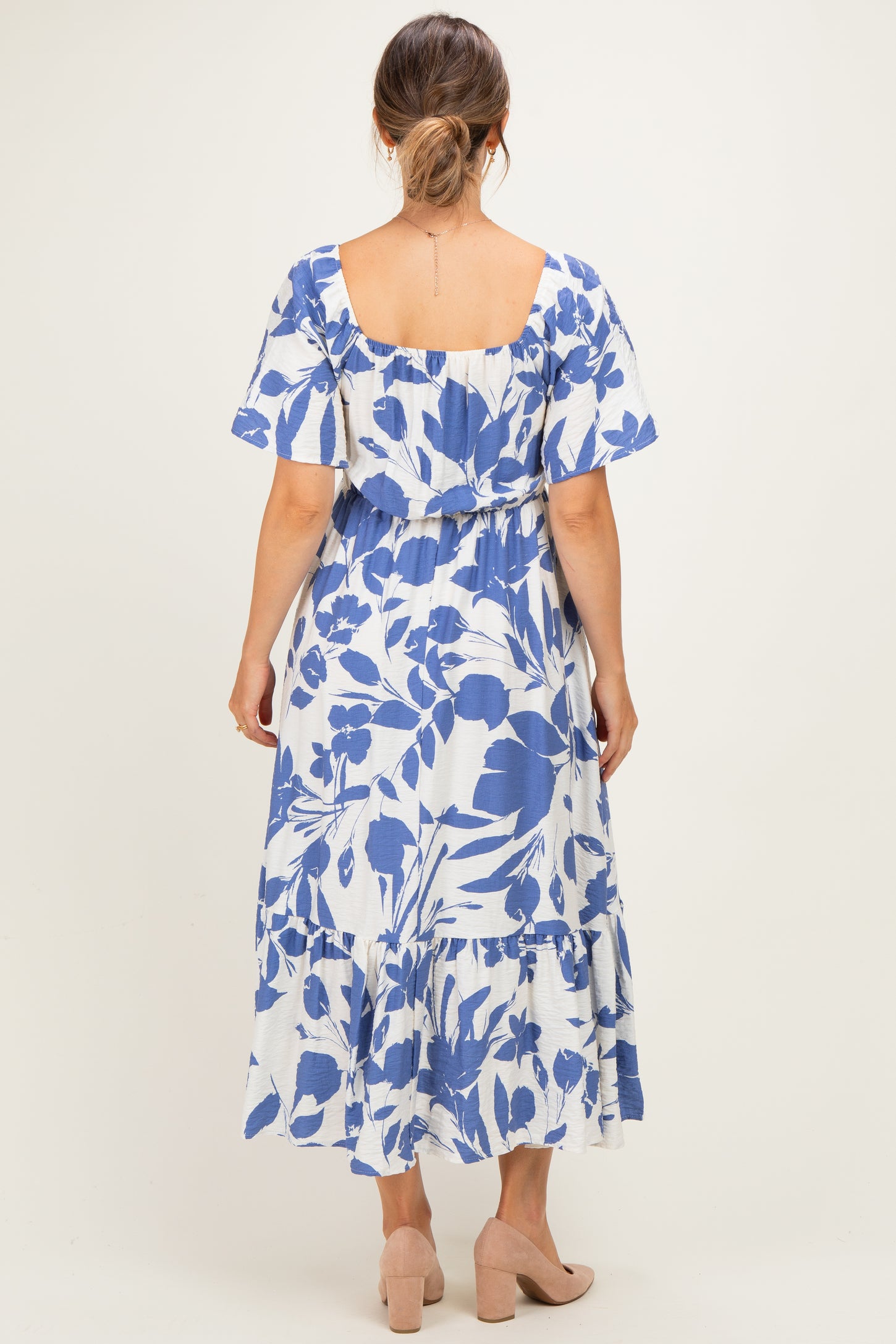 woman wearing a blue and white floral print maternity dress with short sleeves and a tiered skirt, showing a baby bump