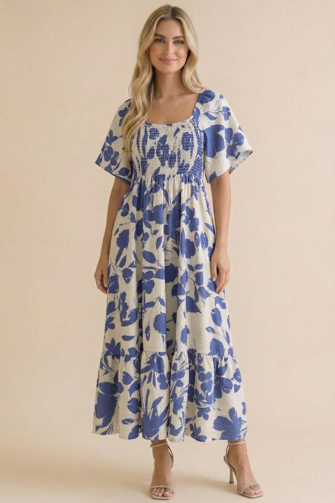 woman wearing a floral print maxi dress with blue and cream colors, short sleeves, and a smocked bodice