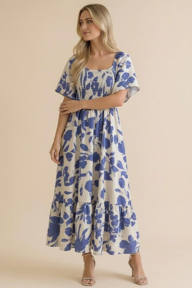 woman wearing a floral print maxi dress in cream and blue with short flutter sleeves and a tiered skirt