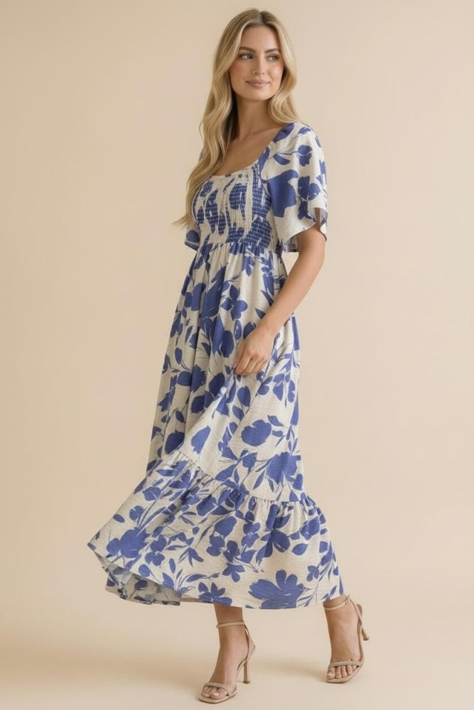 woman wearing a cream floral maxi dress with blue prints and short sleeves, posing against a light background