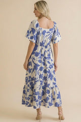 woman wearing a blue and white floral printed maxi dress with short sleeves and a tiered skirt, viewed from the back