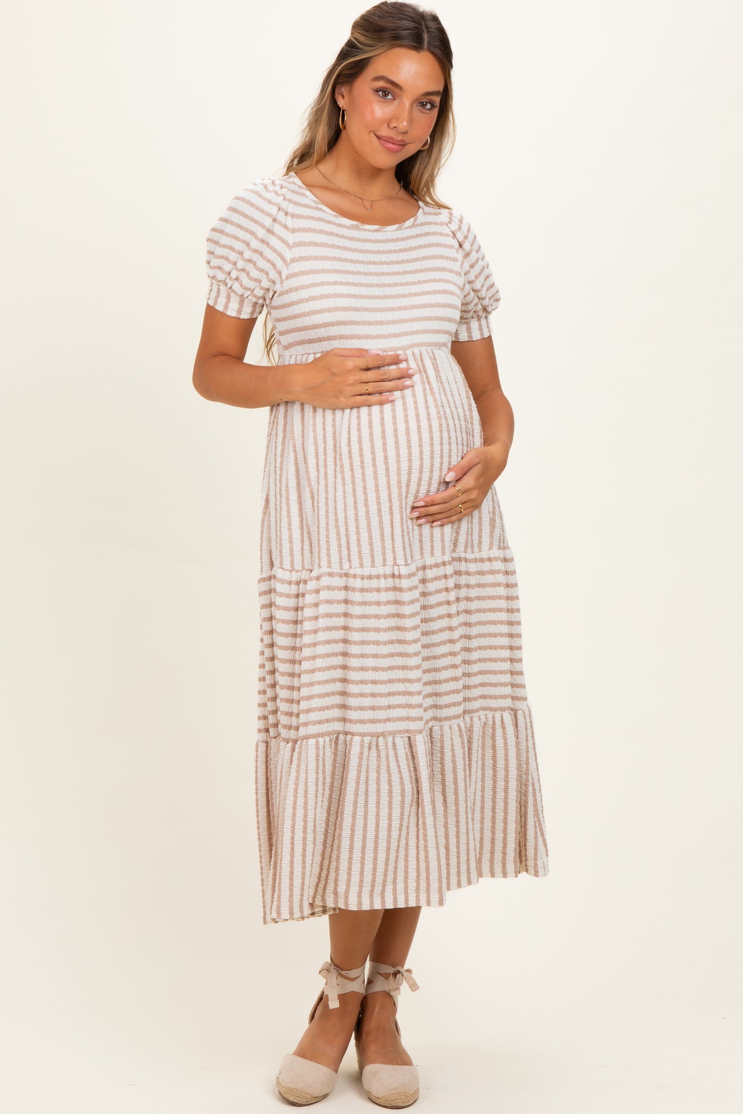 woman wearing a striped maternity midi dress with puff sleeves and holding her baby bump