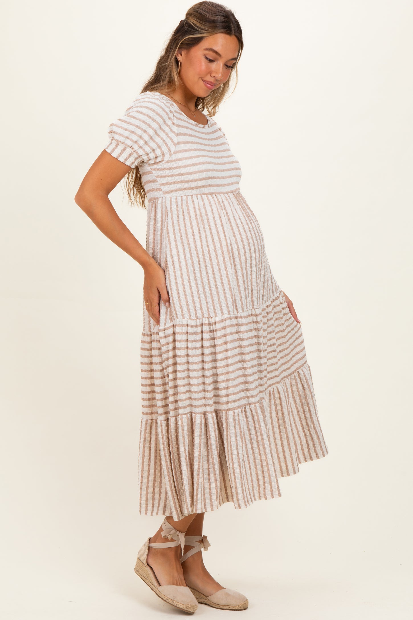 woman wearing a striped maternity dress with short sleeves and tiered skirt, showcasing her baby bump