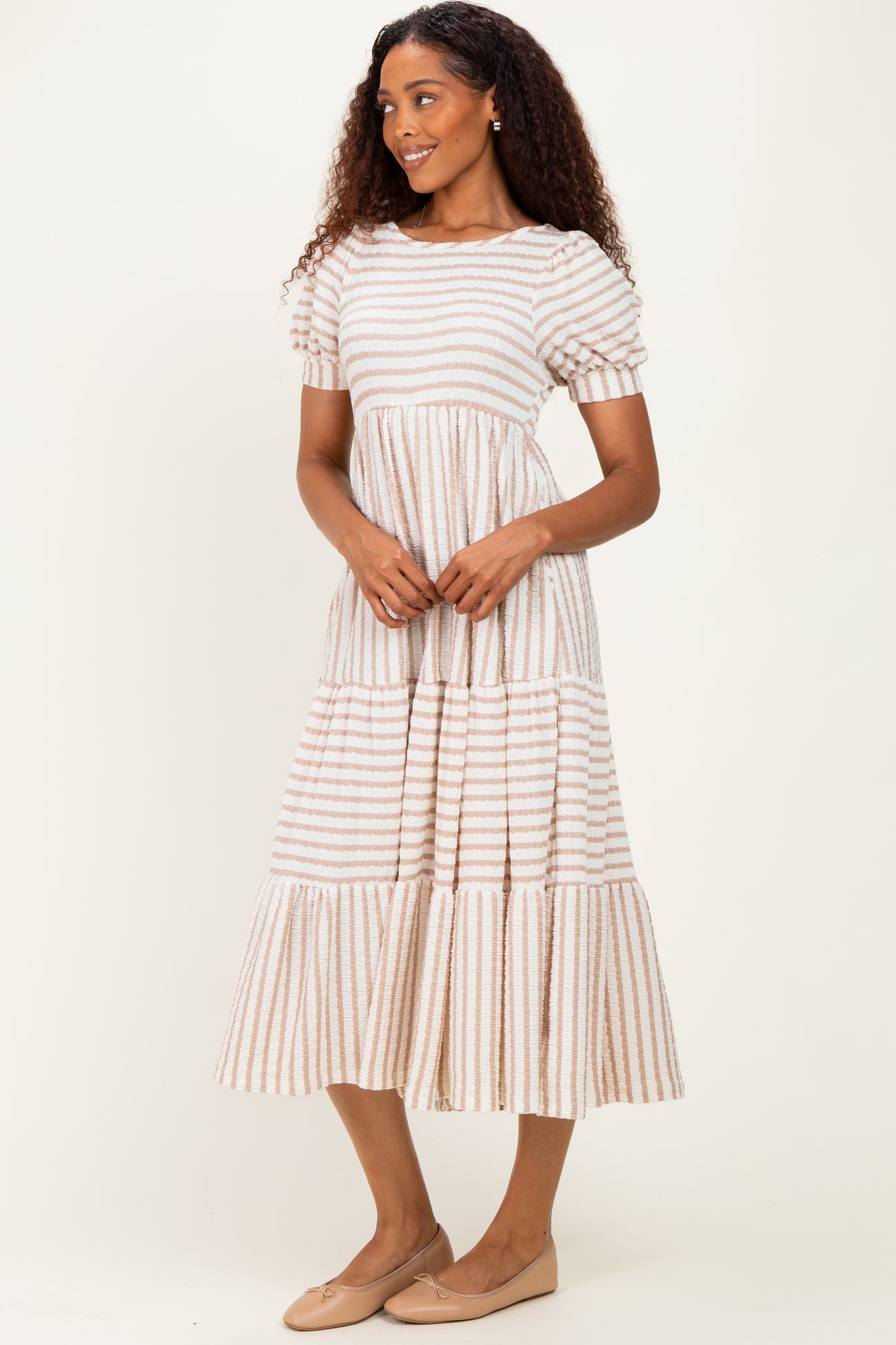 woman wearing a beige striped puff sleeve midi dress with tiered layers and flat shoes