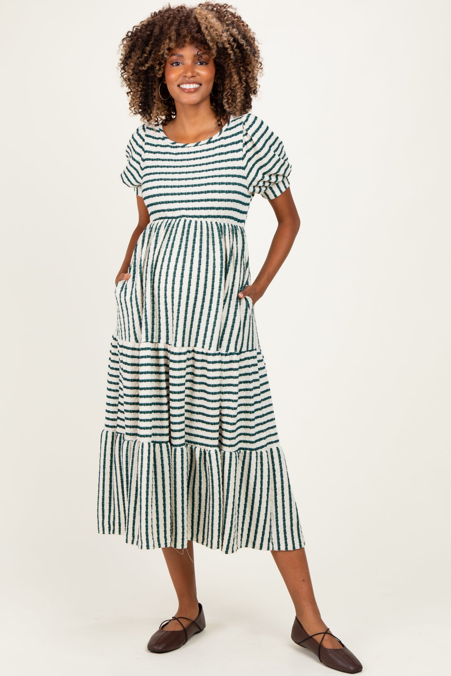 woman wearing a green and white striped maternity maxi dress with a tiered skirt and pockets, showing her baby bump