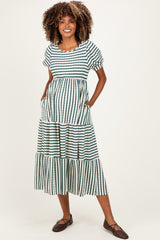 woman wearing a green and white striped maternity maxi dress with a tiered skirt and pockets, showing her baby bump