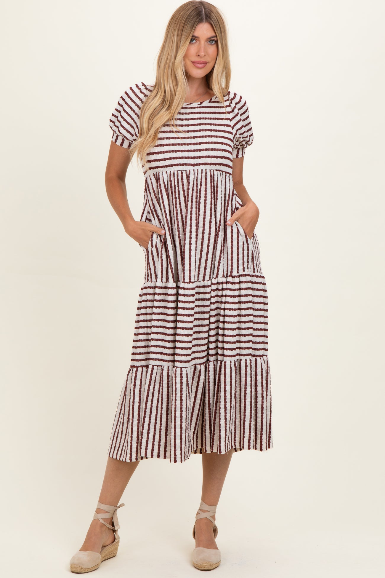 woman wearing a striped tiered midi dress with puff sleeves and pockets, styled with espadrille wedges