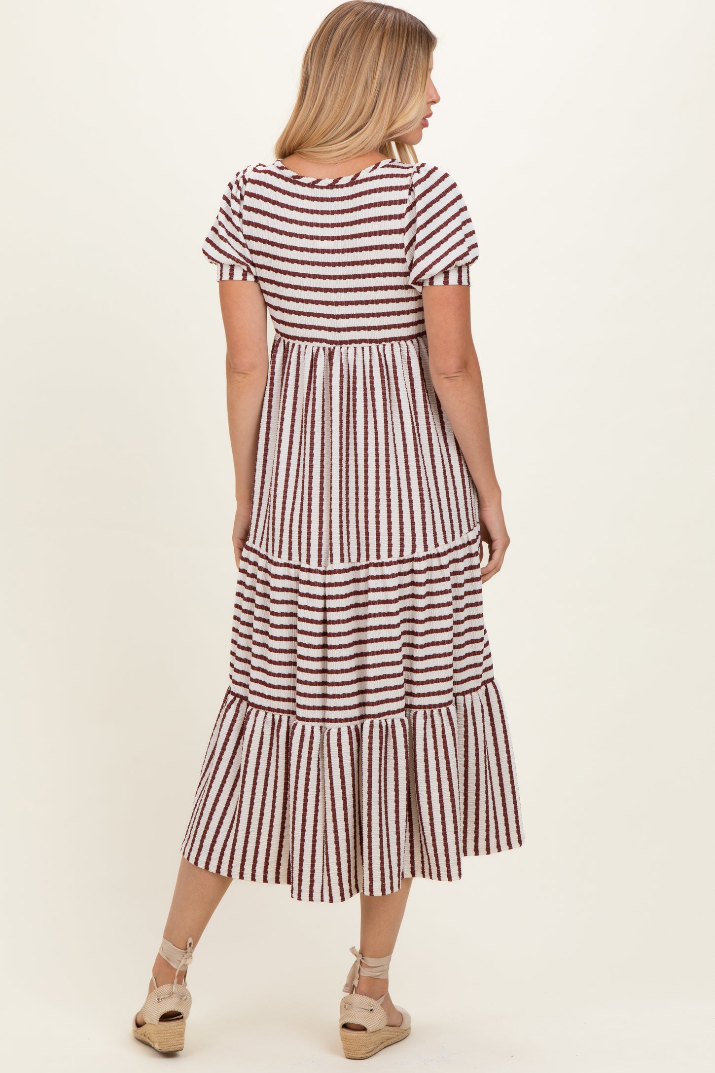 woman wearing a striped tiered midi dress with short sleeves and a flowy silhouette, shown from the back