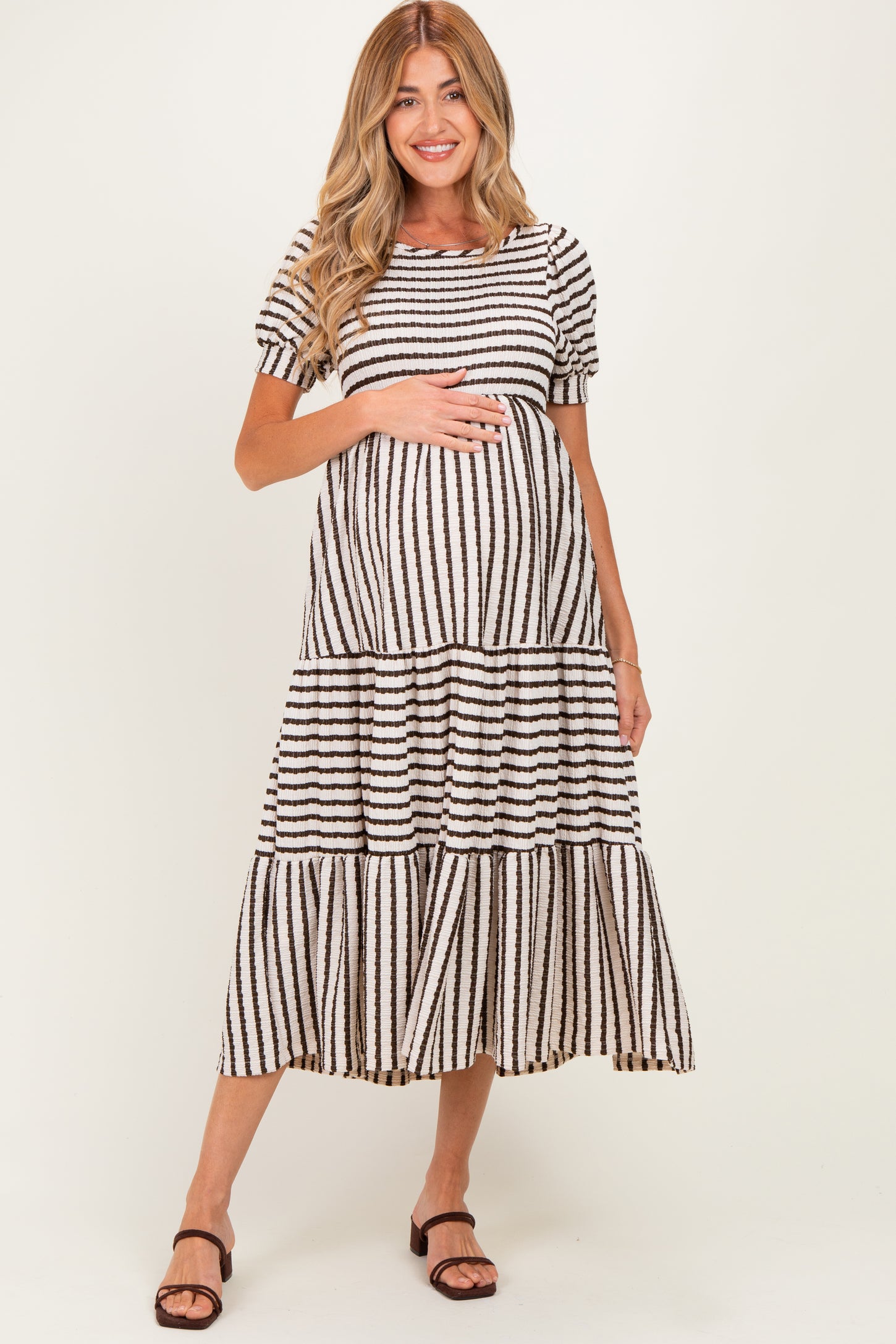 woman wearing a black and white striped maternity maxi dress with tiered ruffles and holding her baby bump