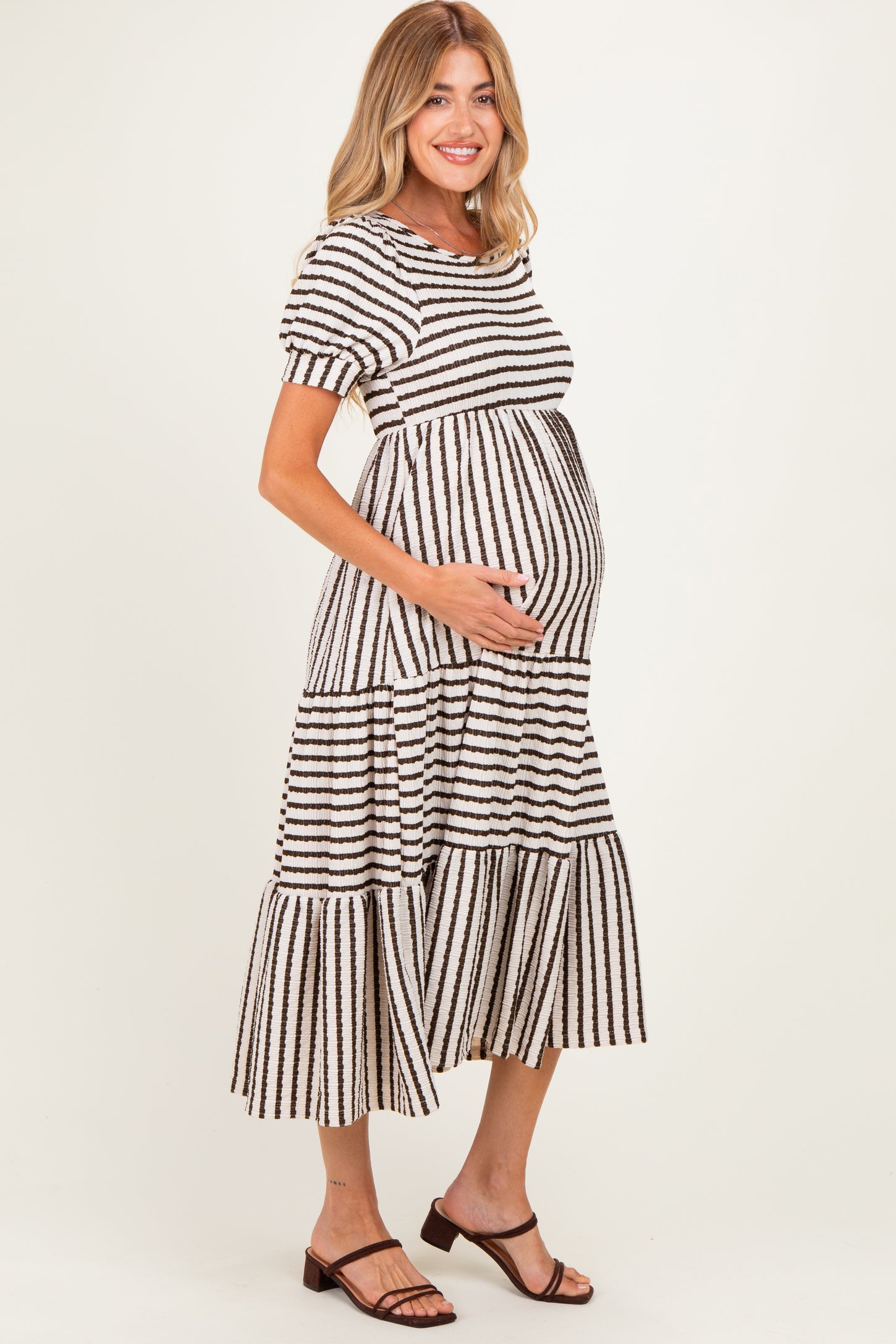 woman wearing a striped tiered maternity dress, showing her baby bump, styled with short sleeves and a relaxed fit