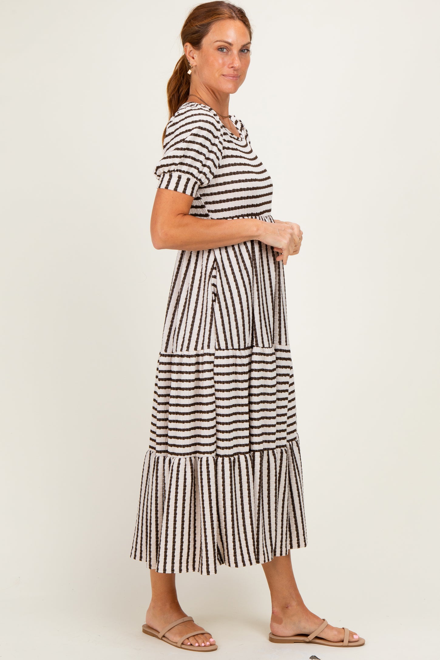 woman wearing a striped midi dress with short sleeves and tiered design, standing sideways and wearing sandals