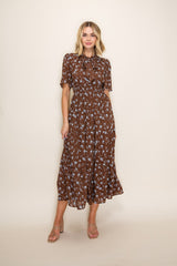 woman wearing a brown floral midi dress with short sleeves and a tie neck detail