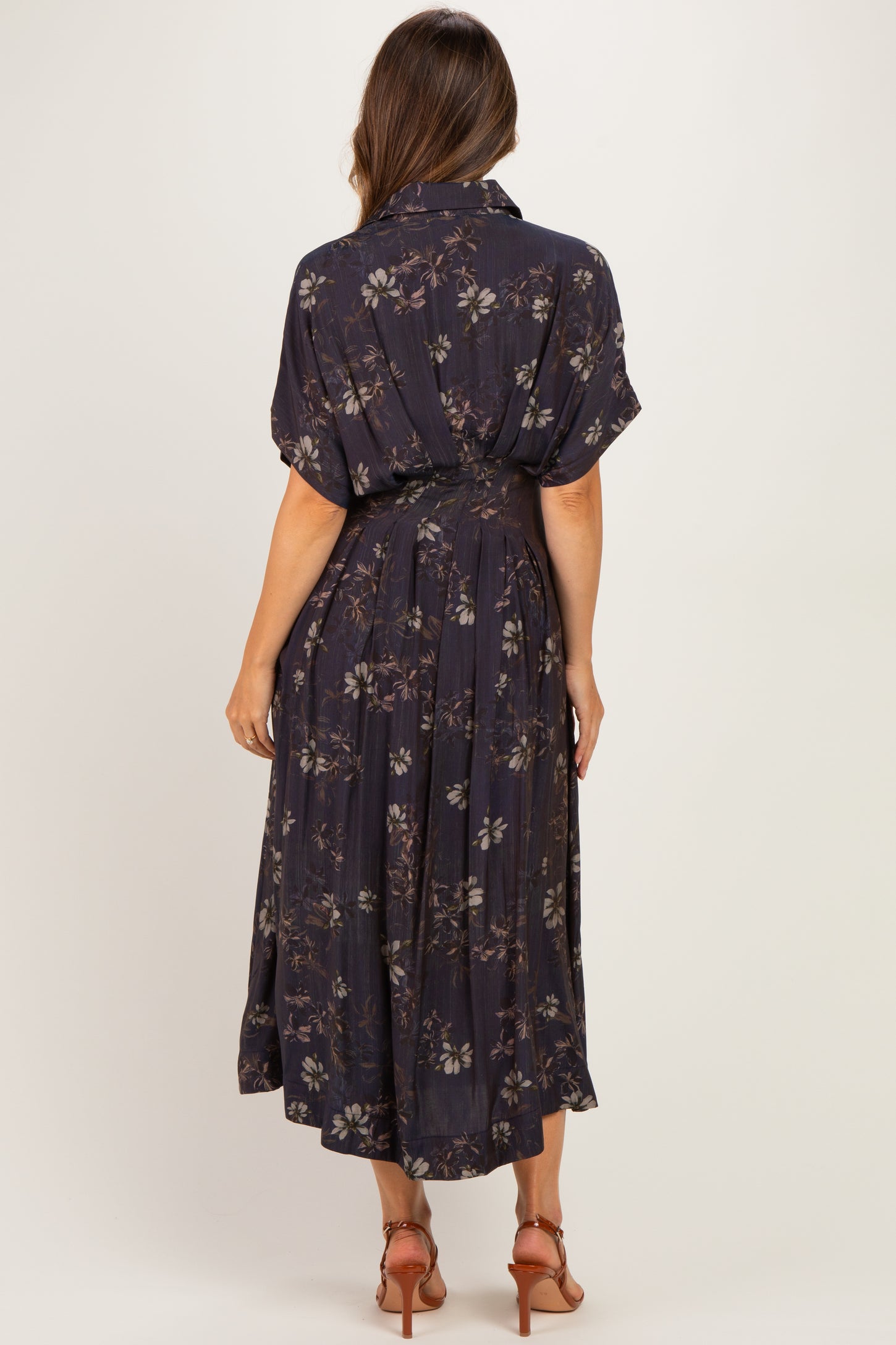 woman wearing a navy floral maternity dress with short sleeves and a gathered waist, showing her baby bump from the back