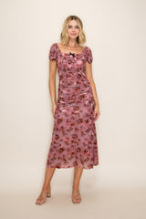woman wearing a pink floral midi dress with puff sleeves and ruching, styled with strappy sandals.