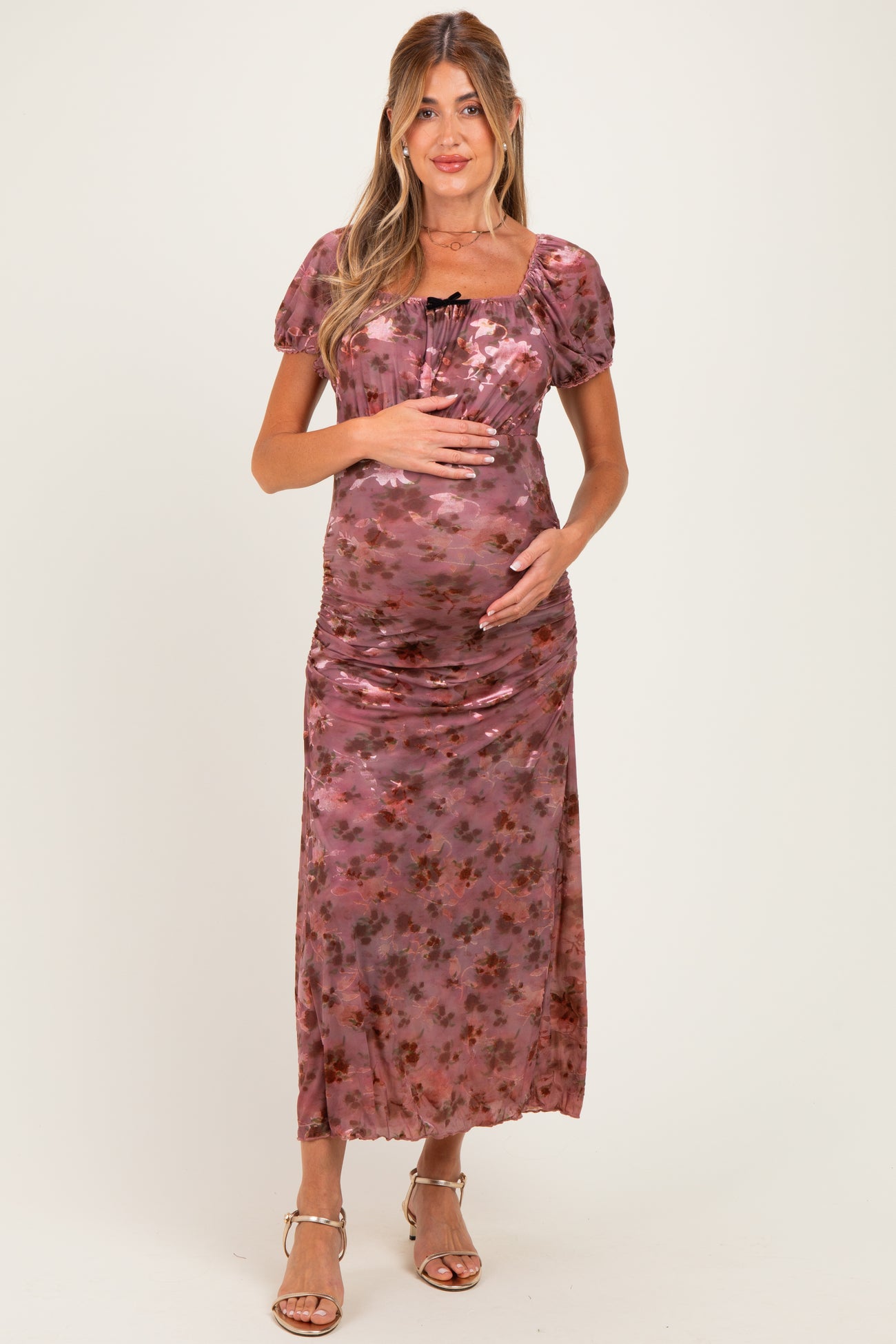 woman wearing a floral print maternity dress with short puff sleeves and a fitted bodice, cradling her baby bump