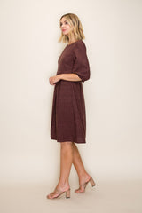 woman wearing a maroon short sleeve dress with a textured pattern and flowing skirt, styled with beige heels