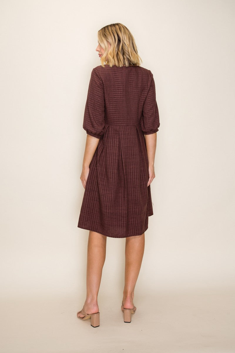 woman wearing a brown textured dress with puff sleeves and a flared skirt, shown from the back