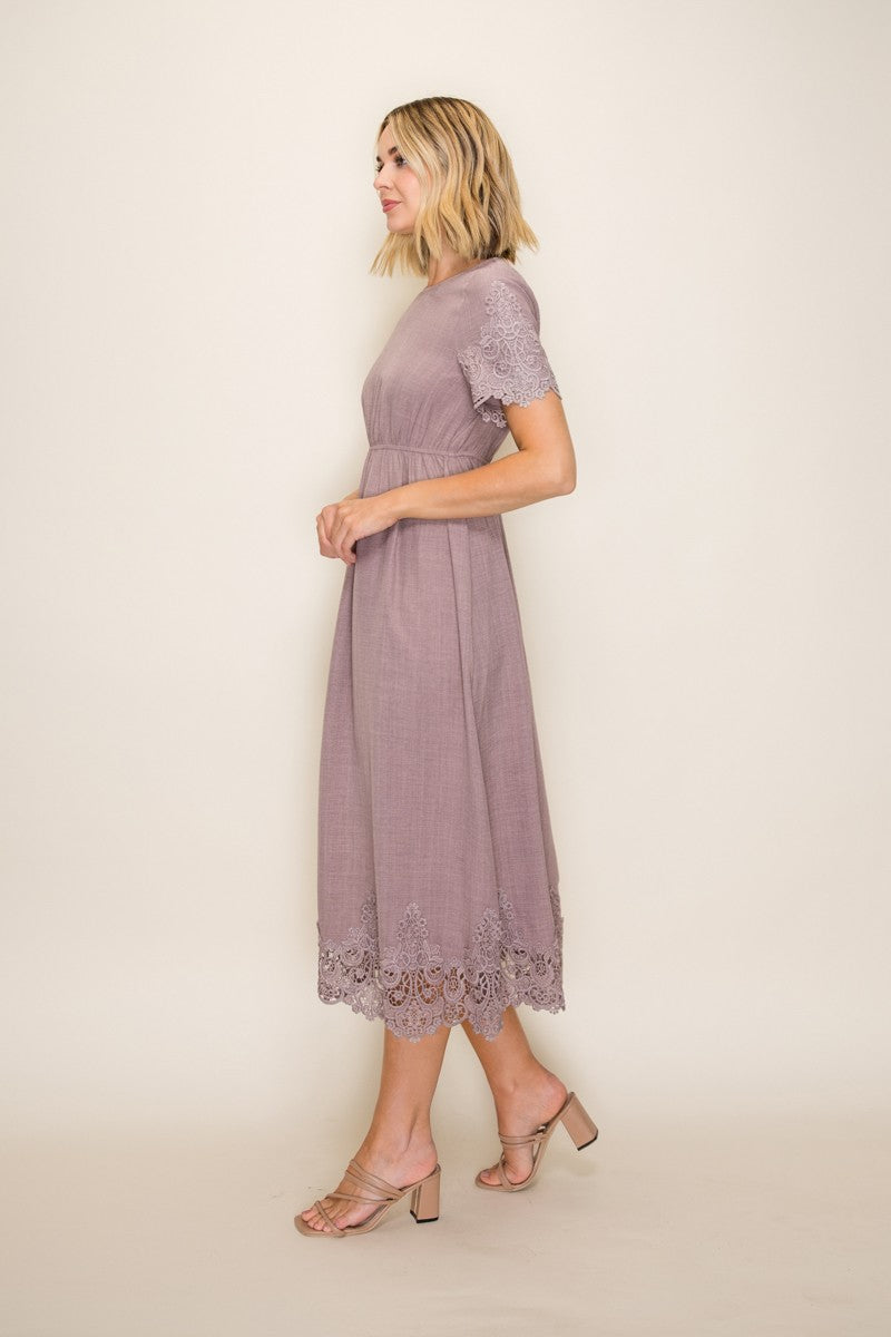 woman wearing a mauve midi dress with lace details at the hem and short sleeves, paired with strappy heels