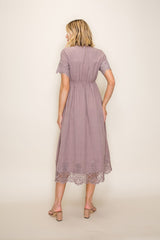 woman wearing a mauve midi dress with lace detailing on the sleeves and hem, showing the back view