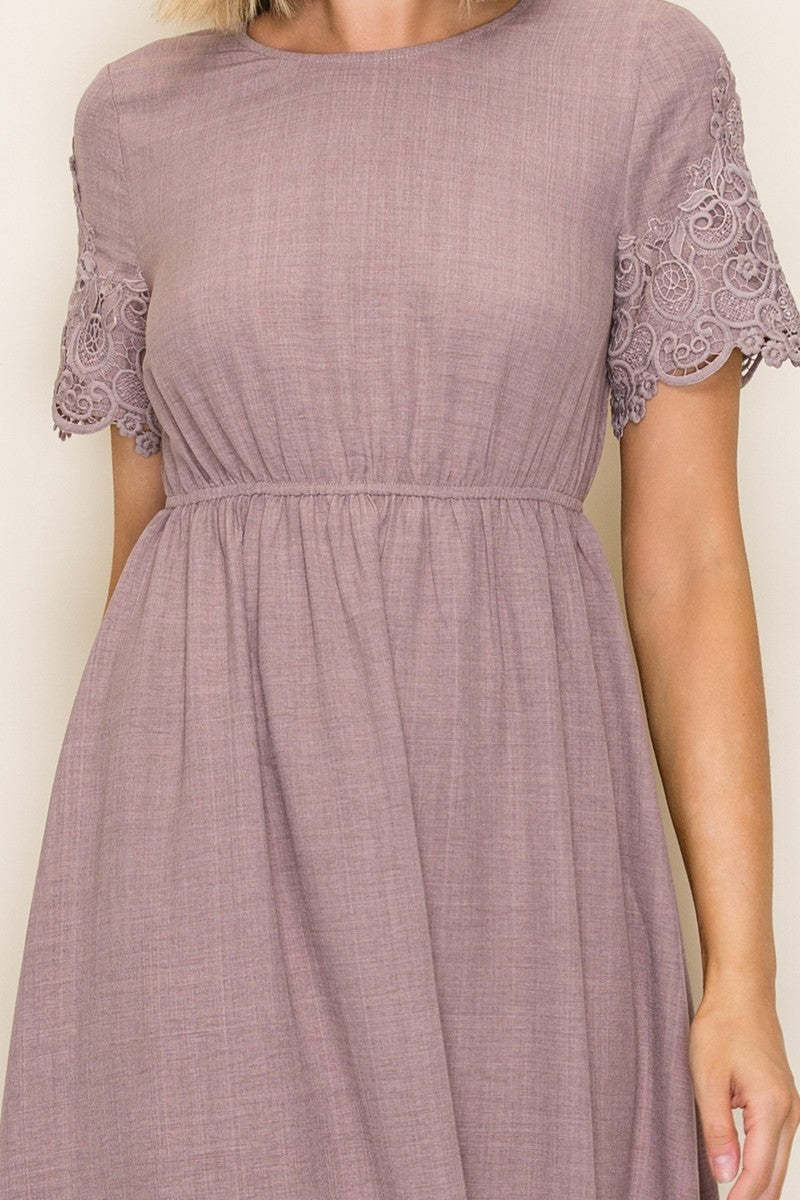 woman wearing a mauve short sleeve dress with lace detailing on the sleeves and a gathered waistline