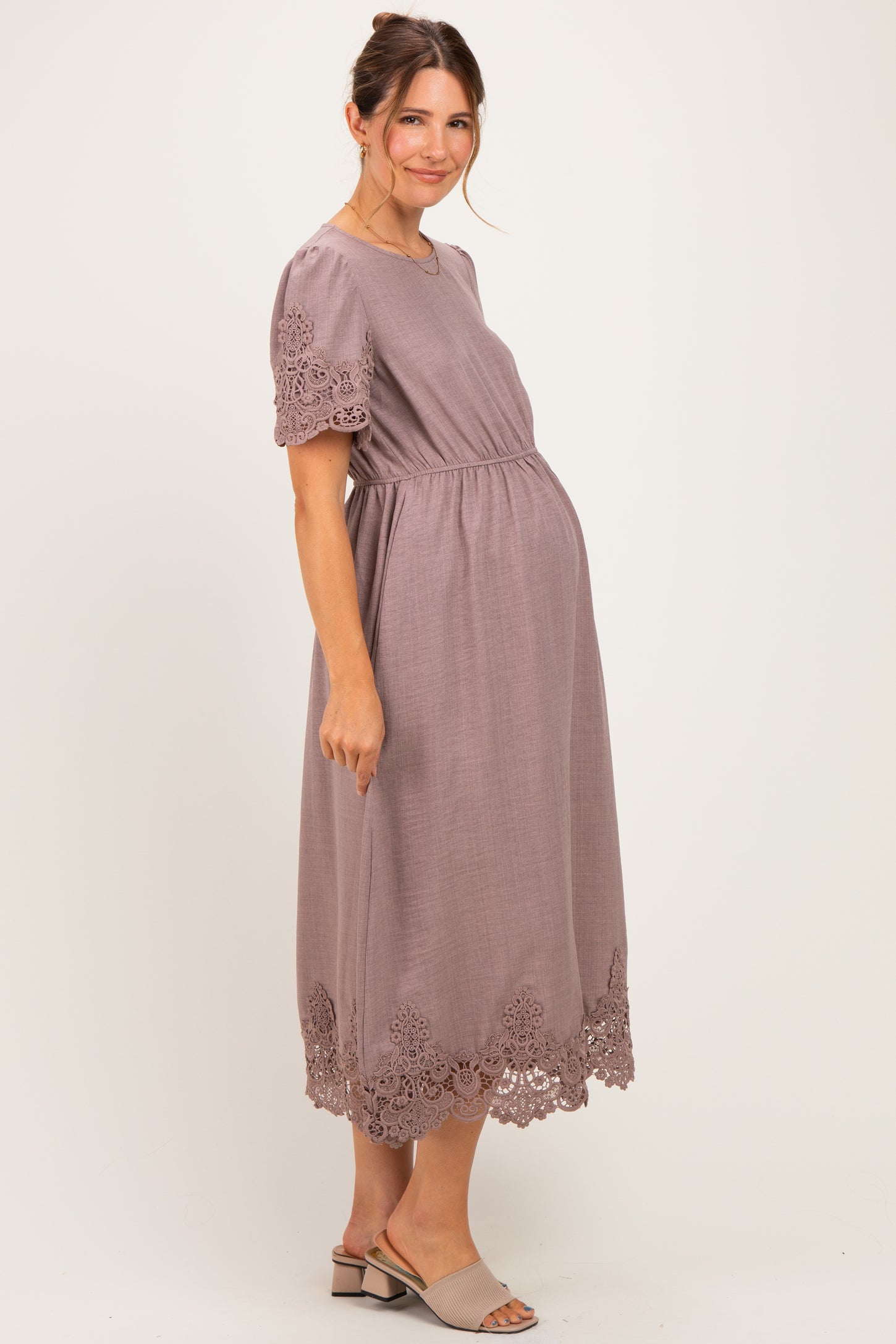 woman wearing a dusty rose maternity dress with lace trim and a visible baby bump