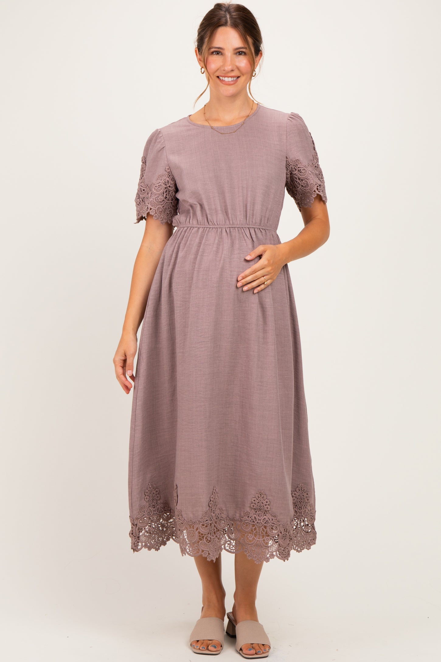 woman wearing a mauve maternity dress with short puff sleeves and lace trim, holding her baby bump