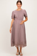 woman wearing a mauve maternity dress with short puff sleeves and lace trim, holding her baby bump