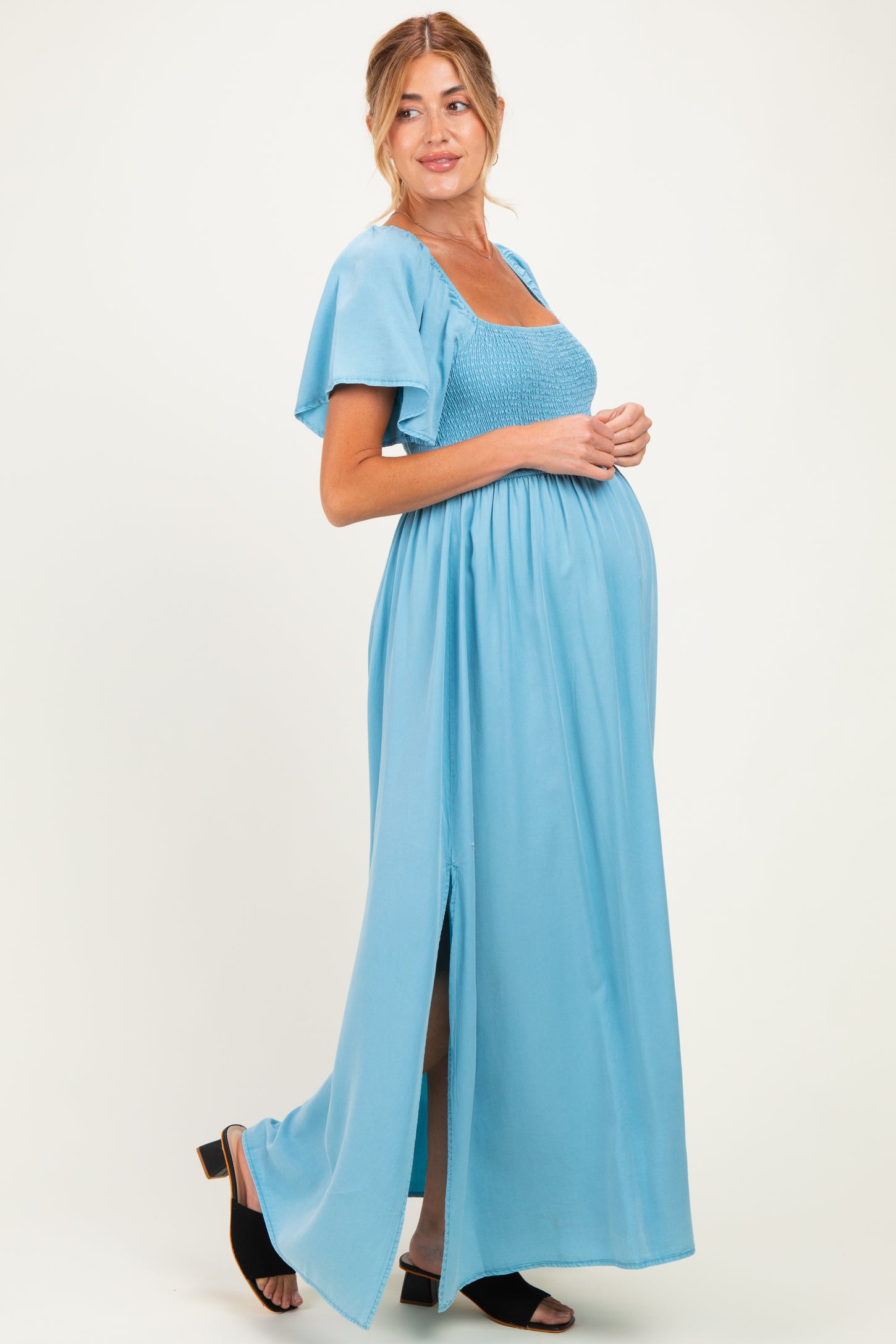 woman wearing a light blue maternity maxi dress with a smocked bodice and flutter sleeves, showing her baby bump