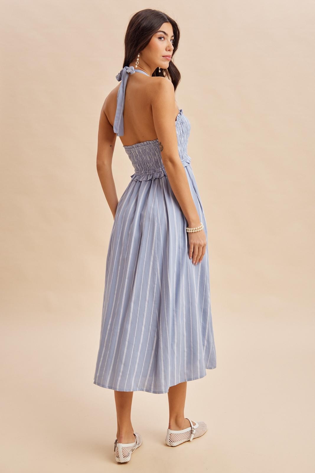 woman wearing a light blue striped dress with a smocked bodice and open back, standing with her back to the camera