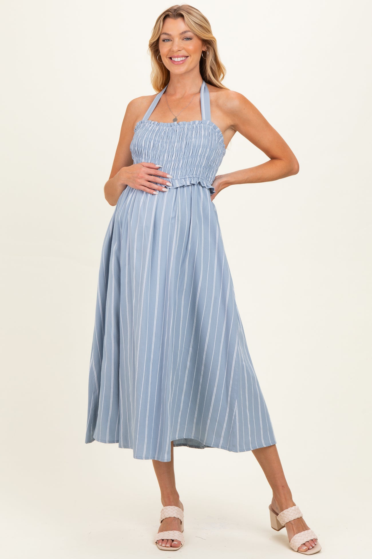 woman wearing a light blue striped maternity dress with a smocked bodice and halter neck, holding her baby bump